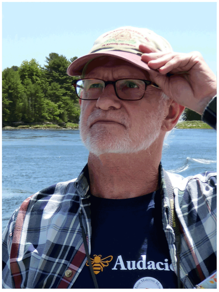 Frank Linton standing near a lake holding the brim of his baseball cap